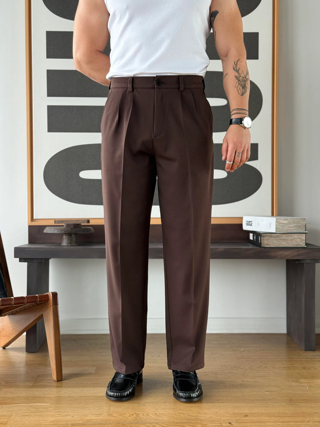 Person wearing brown pants standing in a room with a wooden bench and abstract art on the wall.